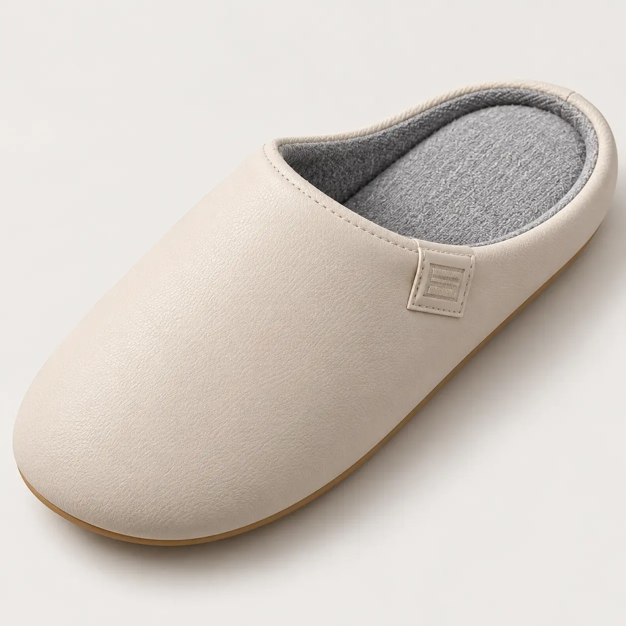 Gros plan sur un chausson beige, son intérieur textile gris, son bord cousu et son dessus synthétique grainé.