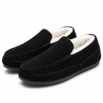 Paire de chaussons mocassins noirs à talon fermé, avec coutures apparentes et doublure claire.
